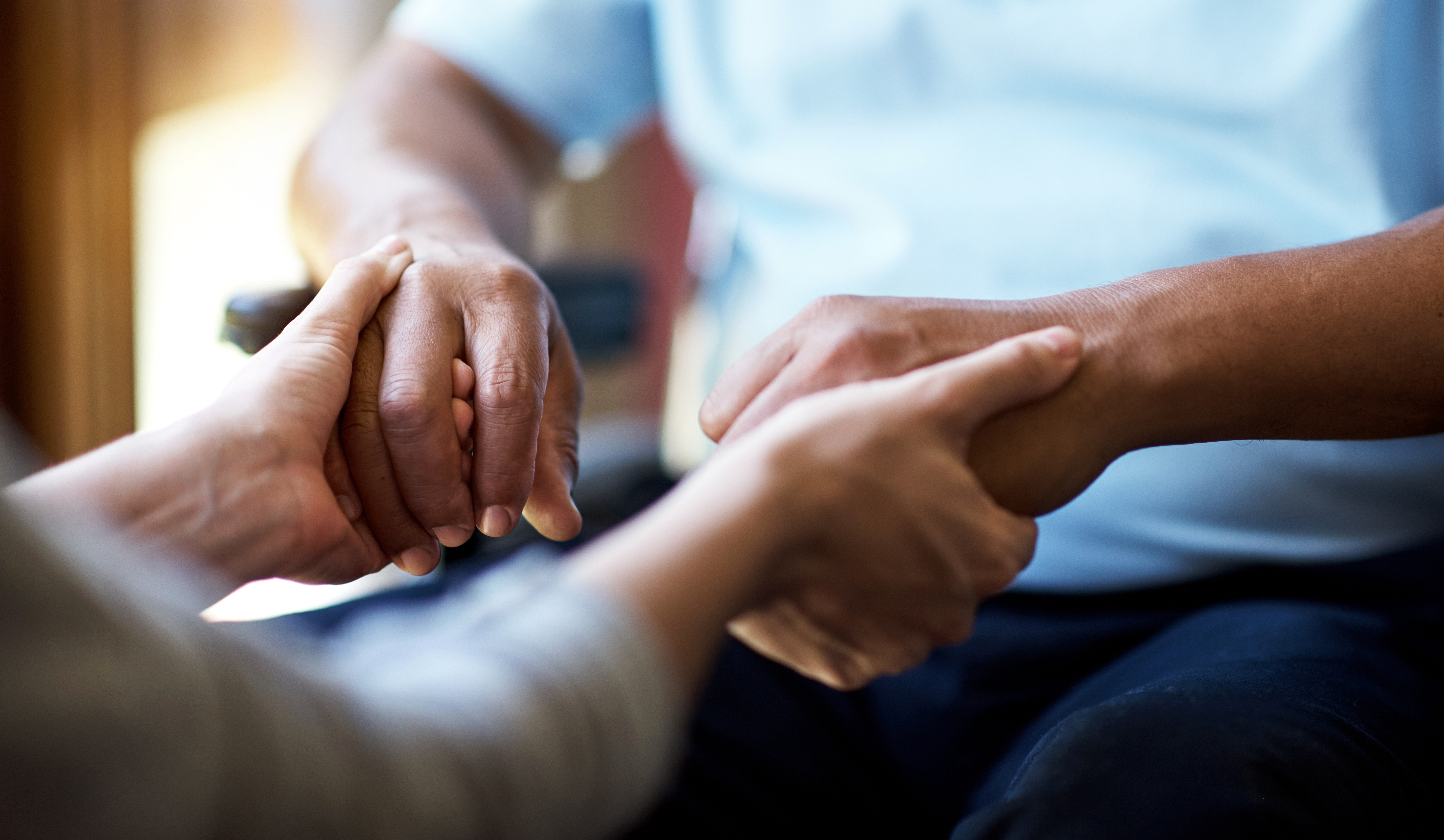 Close up of hands of a person in a wheelchair holding hands with what looks to be a caregiver.